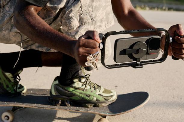 Hand holding iPhone 16 with a mobile filmmaker cage with an on-camera shotgun microphone for footage.