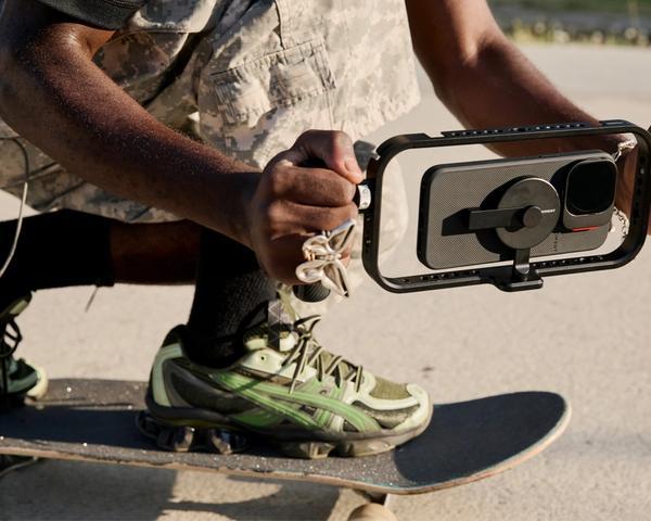 Hand holding iPhone 16 with a mobile filmmaker cage with an on-camera shotgun microphone for footage.